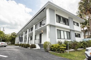 A modern two-story building with a flat roof, large windows, and a balcony on the second floor.