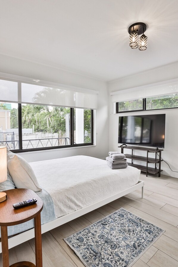 A modern bedroom with a large bed, a TV, and a view of the outdoors.