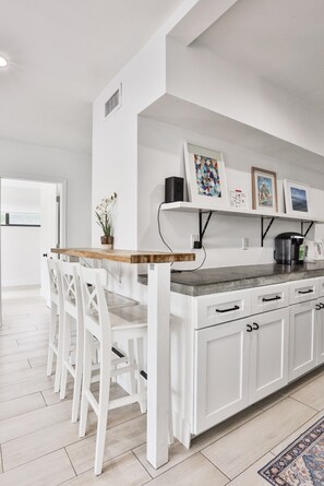 Une cuisine moderne avec des meubles blancs, une table à manger en bois et un îlot central intégré.