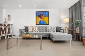 A modern living room with a grey sectional sofa, a glass coffee table, and a painting on the wall.