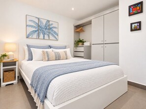A bedroom with a bed, bedside table, lamp, and wall art. - Beachfront Gem Isla Verde Walk 2 Eat W/D (Carolina)