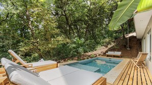 A wooden deck with lounge chairs and a small pool surrounded by lush greenery. - Treehouse Hideaway in Tamarindo Jungle with Pool & Open-Air Living Room (Tamarindo)