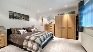 A bedroom with a bed, a dresser, a wardrobe, a mirror, and a window with curtains.
