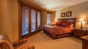 A bedroom with a large bed, two bedside tables with lamps, a chair, and a window with blinds. - Catamount Lodge 214 - Northstar Village (Truckee)