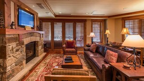 A cozy living room with a stone fireplace, leather sofa, and a television mounted above it. - Catamount Lodge 214 - Northstar Village (Truckee)