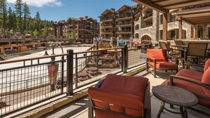 Un balcon avec des chaises et des tables rouges, donnant sur une zone de station de ski, avec des bâtiments et des arbres.