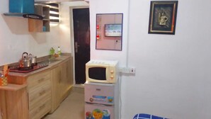 A compact kitchen with wooden cabinets, a microwave, and a small refrigerator. - Aji  Unique 1BED Studio  (Ijegun, Lagos) (Lagos)