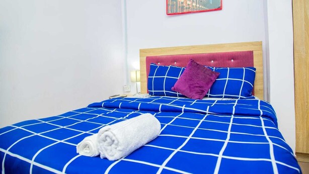A neatly made bed with a blue and white checkered bedspread, a red headboard, and a purple pillow. - Aji  Unique 1BED Studio  (Ijegun, Lagos) (Lagos)