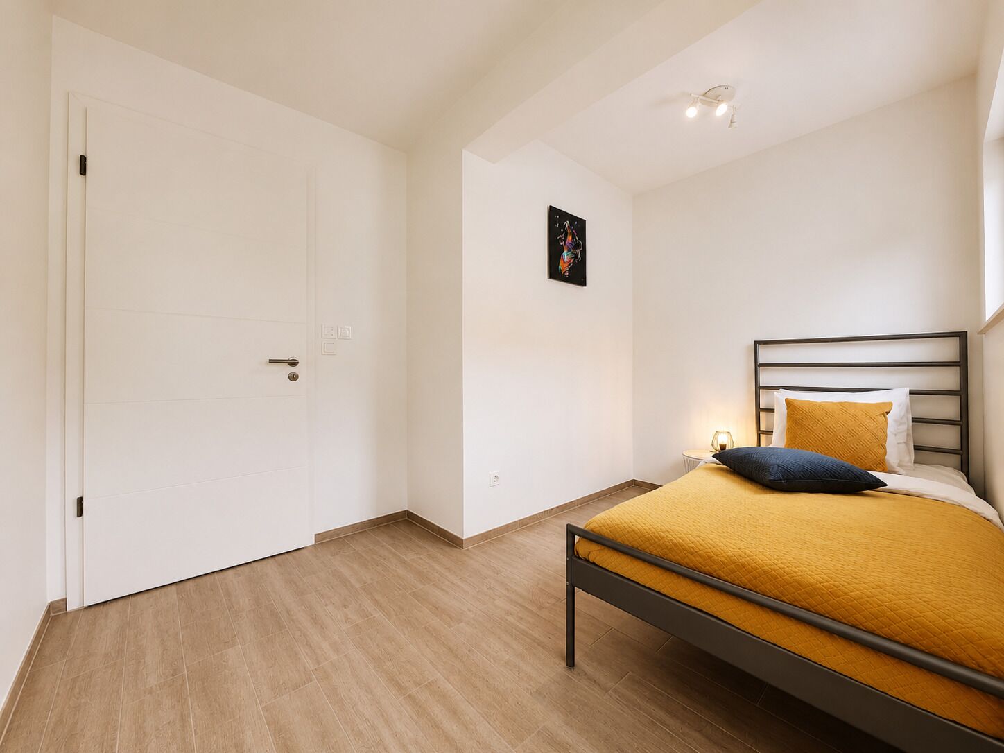 A bedroom with a bed, a door, and a wall-mounted light fixture.