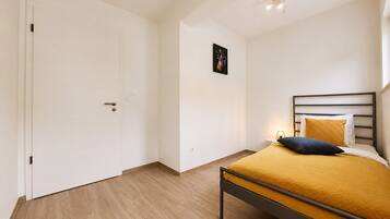 A bedroom with a bed, a door, and a wall-mounted light fixture.