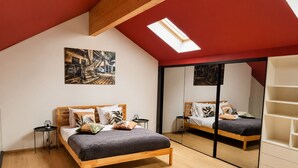 Une chambre avec un puits de lumière, un lit recouvert d’une couverture sombre, une tête de lit en bois et un grand miroir.