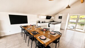 Une cuisine moderne avec des meubles blancs et un plan de travail noir, un coin repas avec une table en bois et des chaises noires, et une grande fenêtre donnant sur l’extérieur.