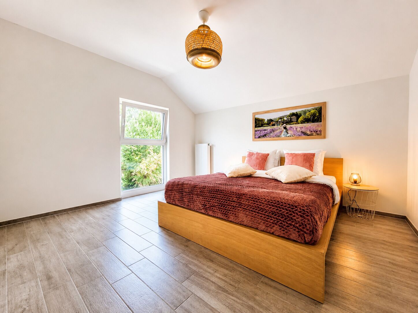 A bedroom with a large bed, a window, a painting, and a lamp.