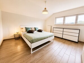 A bedroom with a bed, bedside table, dresser, and a window.