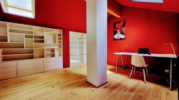 Une pièce avec un mur rouge, un bureau blanc, une chaise et une lucarne.