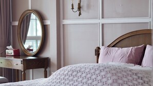 Ein Schlafzimmer mit einem großen Bett, einem runden Spiegel, einem Nachttisch mit Taschentuchbox und einer Wandleuchte.