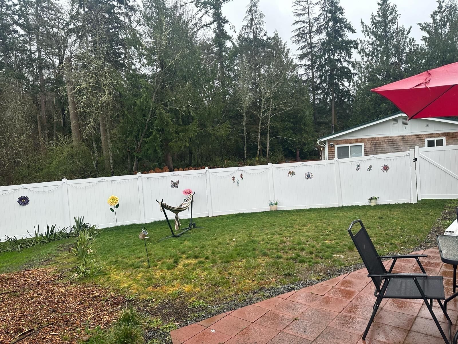 A backyard with a white fence, a hammock, and a patio area with a table and chairs.