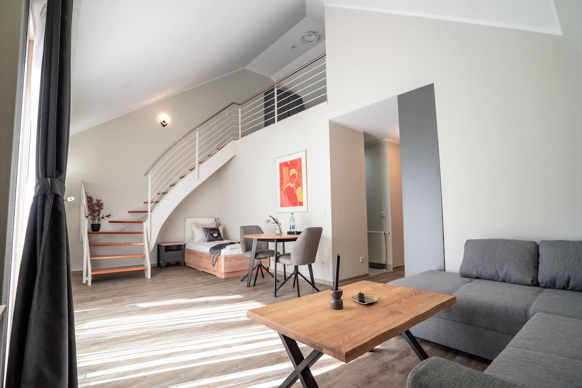 Ein modernes Wohnzimmer mit Couchtisch aus Holz, grauem Sofa und einer Treppe, die zu einer oberen Ebene führt.