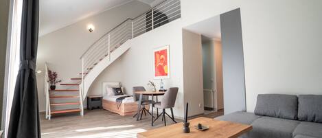 Una sala de estar moderna con una mesa de centro de madera, un sofá gris y una escalera que sube a un nivel superior.