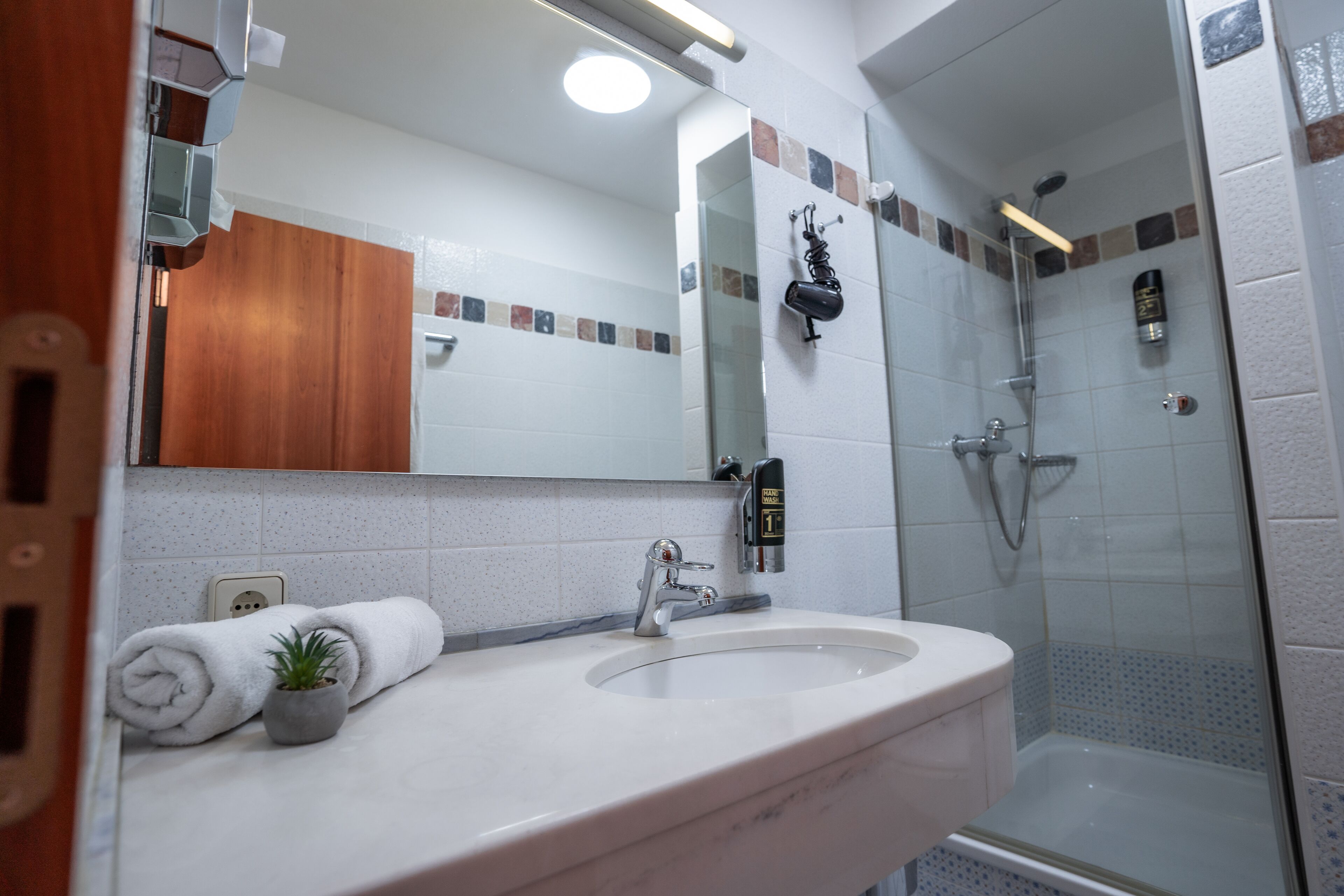A bathroom with a sink, mirror, towel, and shower.