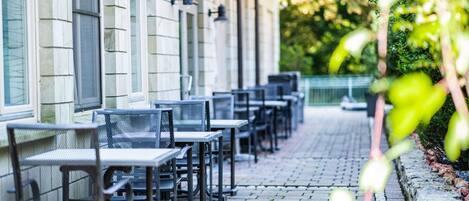 A row of outdoor tables and chairs aligned against a building with large windows.