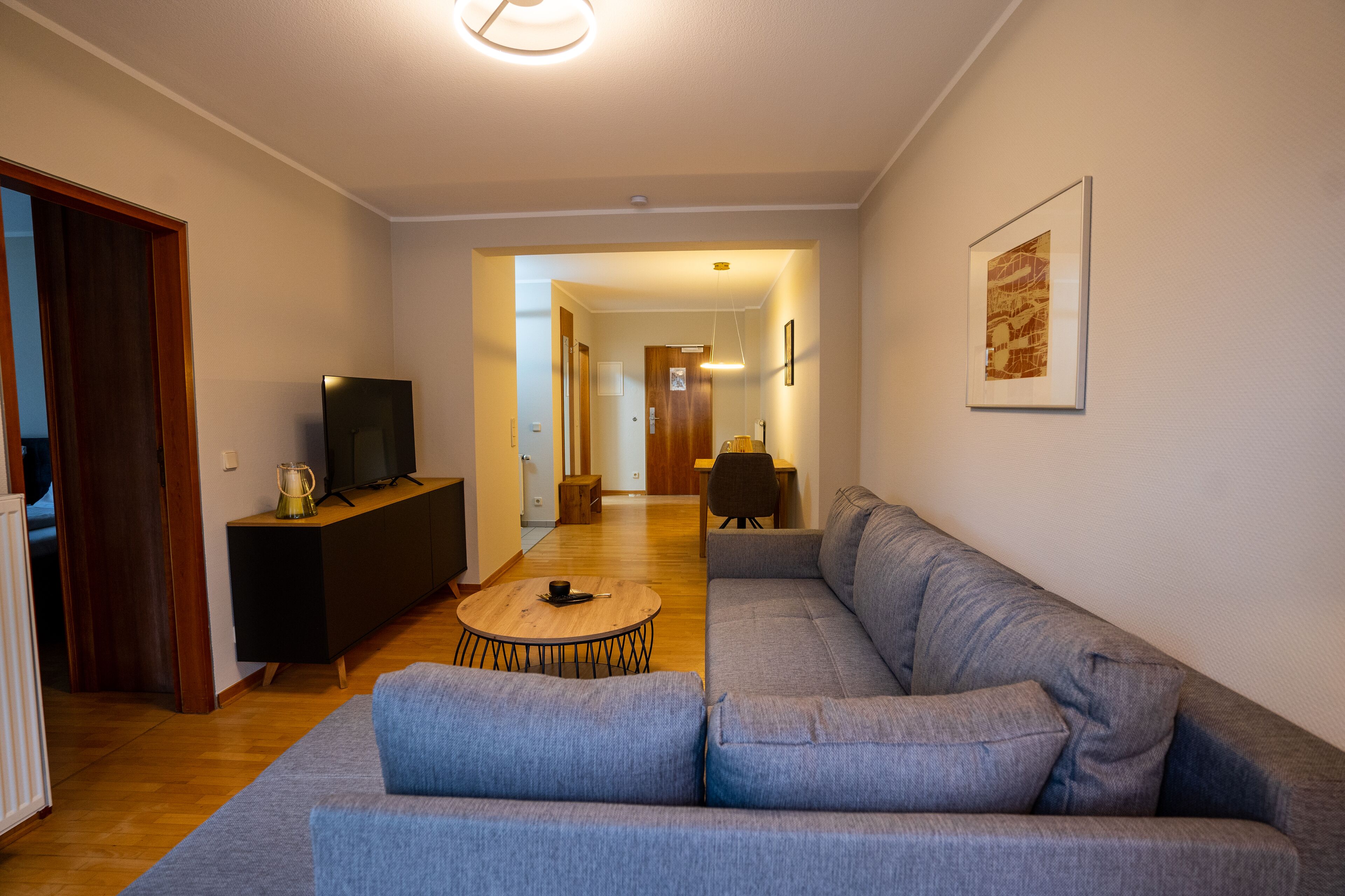 A modern living room with a grey sofa, a wooden coffee table, and a TV on a black stand.