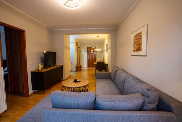 Una sala de estar moderna con un sofá gris, una mesa de centro de madera y un televisor sobre un soporte negro.