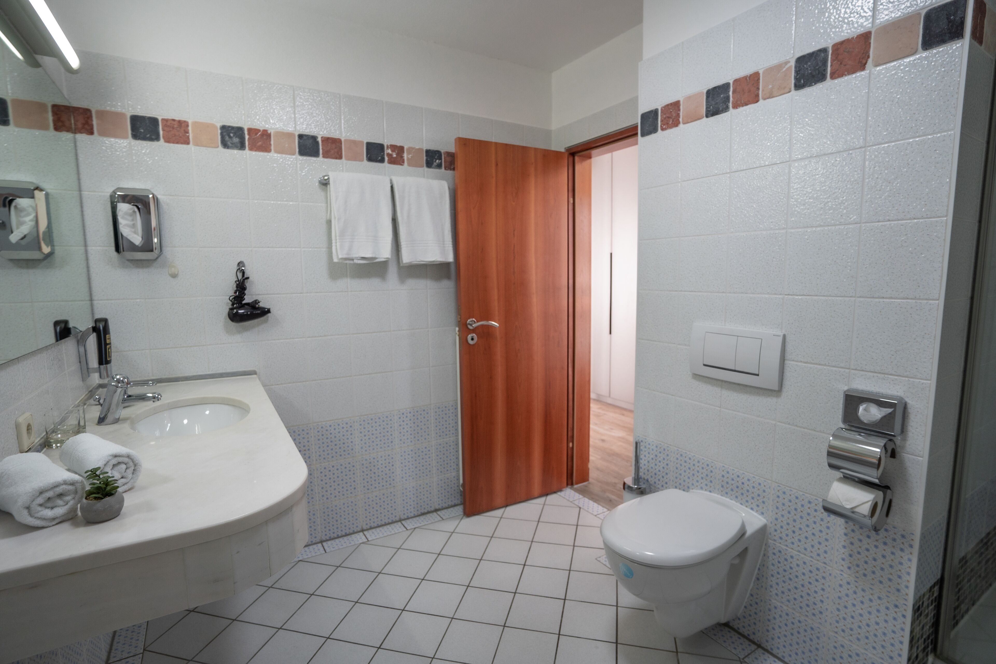 Une salle de bain équipée d’un lavabo, d’un miroir, d’un distributeur de serviettes et de toilettes.