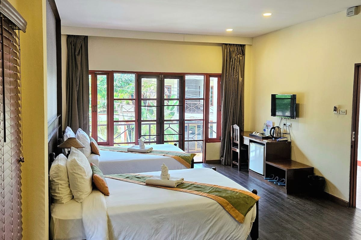Ein Hotelzimmer mit zwei Betten, einem Schreibtisch und einem Fernseher, sowie großen Fenstern.