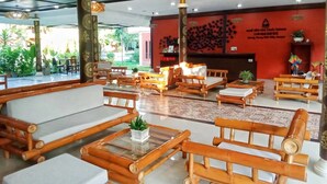 Un hall de hotel con mobiliario de bambú, una mesa de centro de vidrio y una pared roja con un diseño decorativo.