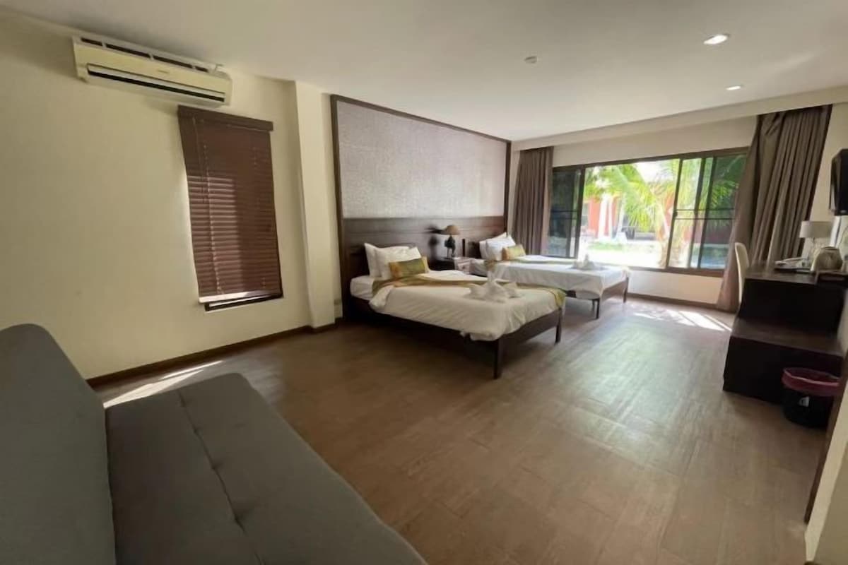 Une chambre d’hôtel avec deux lits, un canapé, un bureau et une grande fenêtre donnant sur des palmiers.