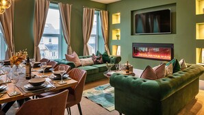 Ein modernes Wohnzimmer mit einem grünen Sofa, einem Essplatz mit Tellern und Gläsern sowie einem Kamin.
