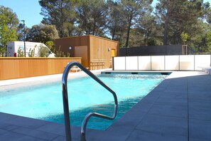 A swimming pool with a metal ladder, surrounded by a wooden fence and a concrete deck.