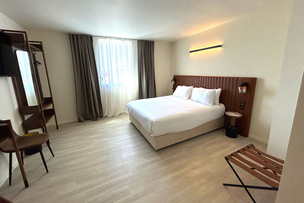 A hotel room with a large bed, a desk, a chair, and a window with curtains.