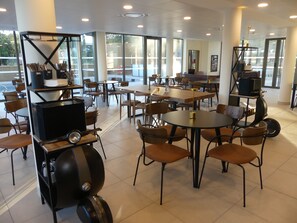 A spacious indoor area with multiple tables and chairs, large windows, and a variety of seating arrangements.