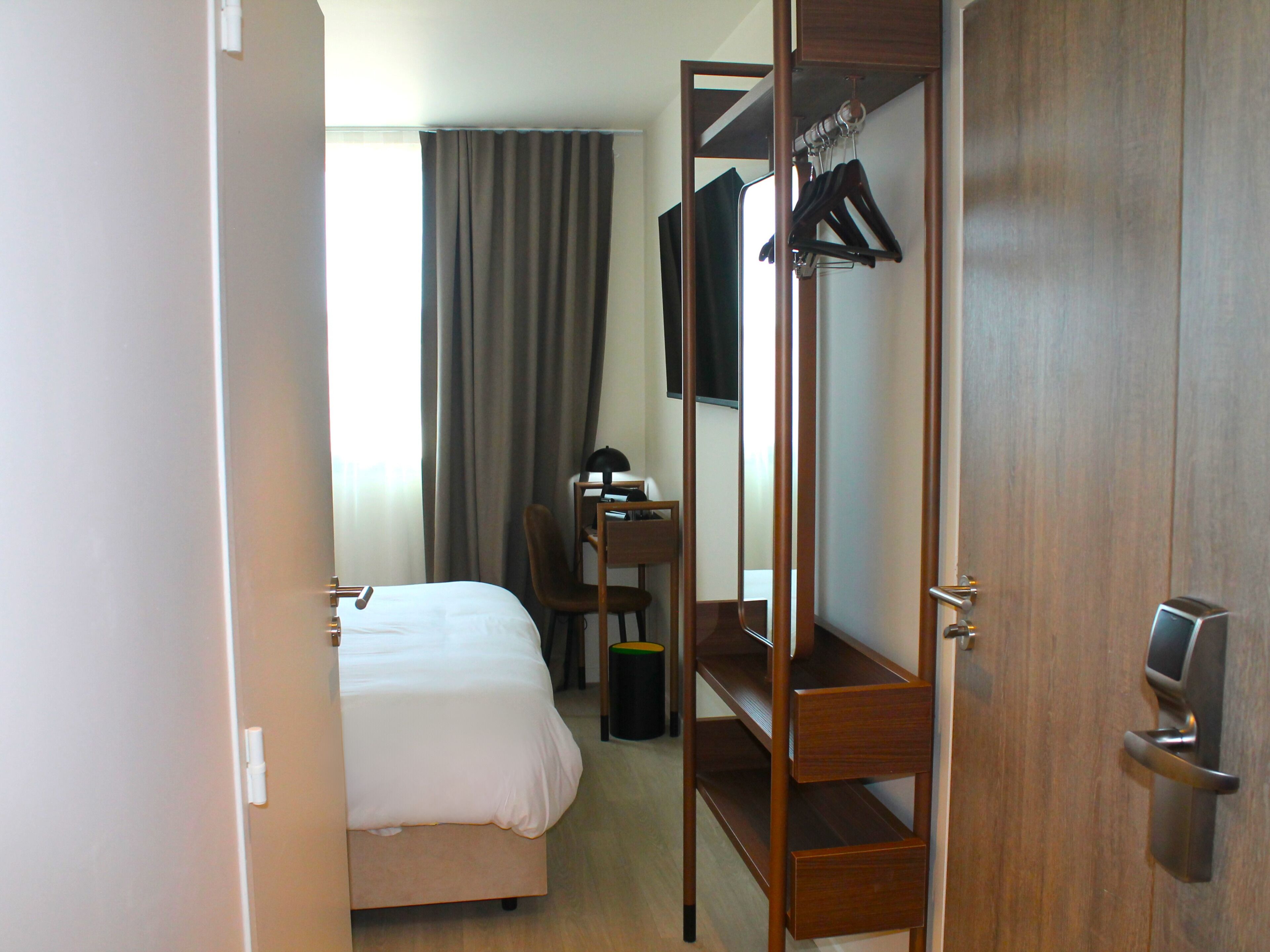 Una habitación de hotel con cama, escritorio, silla, armario y televisor.
