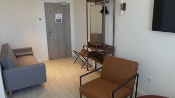 A room with a grey sofa, a brown chair, a wooden door, and a mirror on the wall.