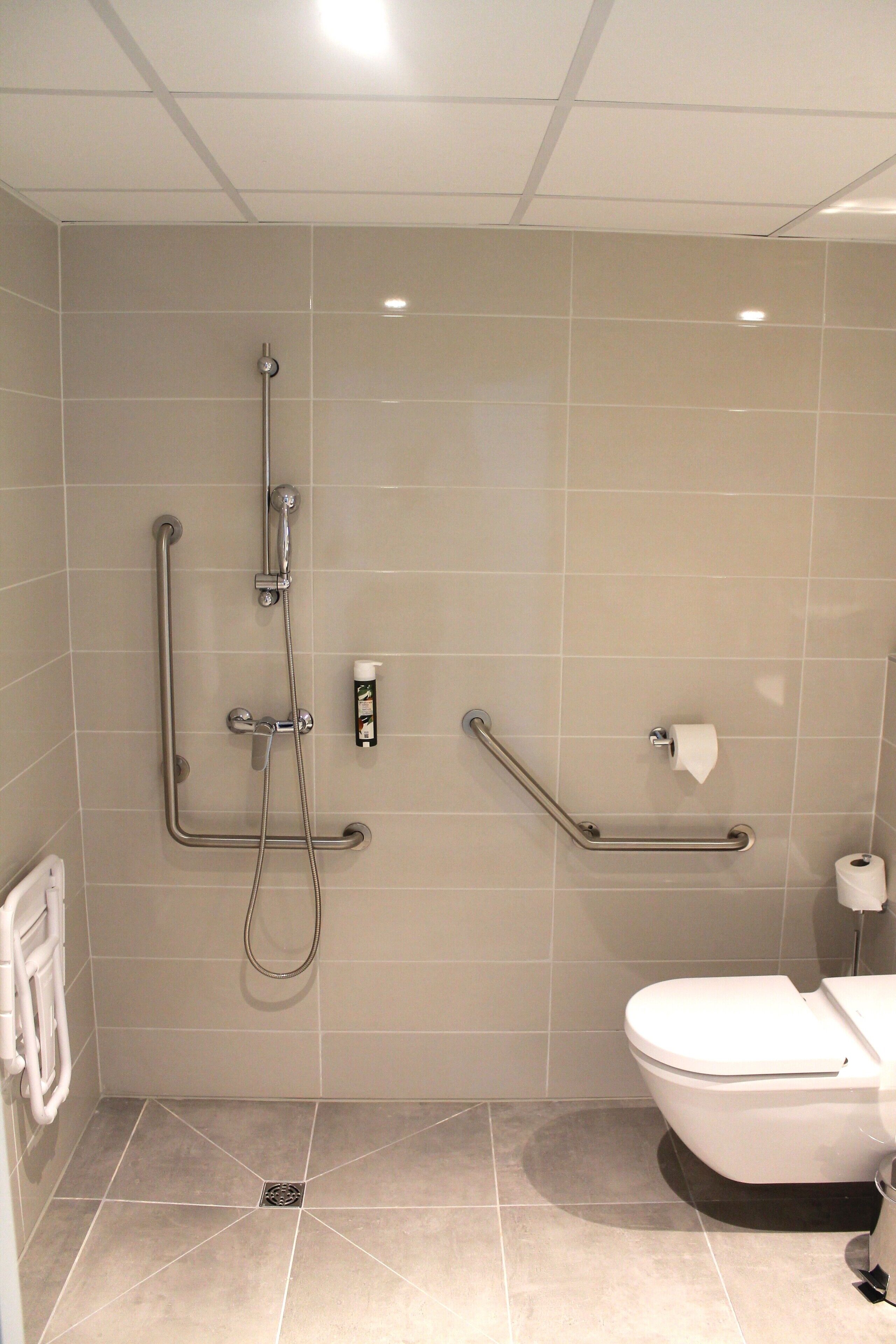 A bathroom with a shower, toilet, and grab bars.
