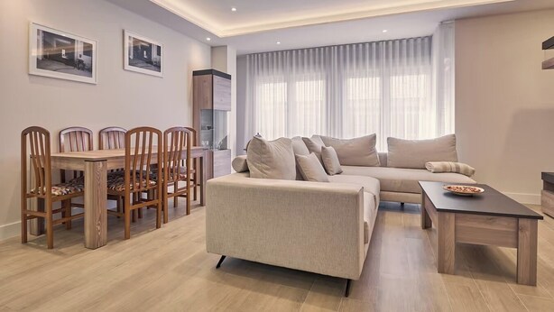 A modern living room with a sofa, a coffee table, and a dining area with chairs and a table.