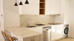 A modern kitchen with white cabinetry, a marble countertop, a built-in dishwasher, and a washing machine.