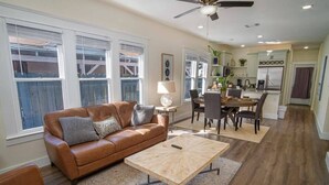 A living room with a brown leather sofa, a wooden coffee table, and a dining area with a table and chairs. - Brand New Craftsman 2BR/2BA Home in Denver Heights (San Antonio)