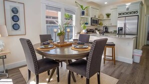 A modern kitchen with white cabinets, a stainless steel refrigerator, and a dining area with a round table and four chairs. - Brand New Craftsman 2BR/2BA Home in Denver Heights (San Antonio)