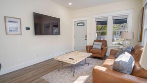 A living room with a brown leather sofa, a wooden coffee table, and a large TV mounted on the wall. - Brand New Craftsman 2BR/2BA Home in Denver Heights (San Antonio)