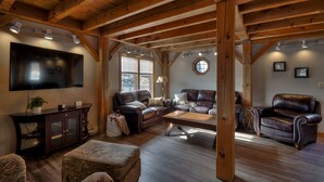 Een ruime woonkamer met houten balken, leren banken, een flatscreen-tv en een groot raam.