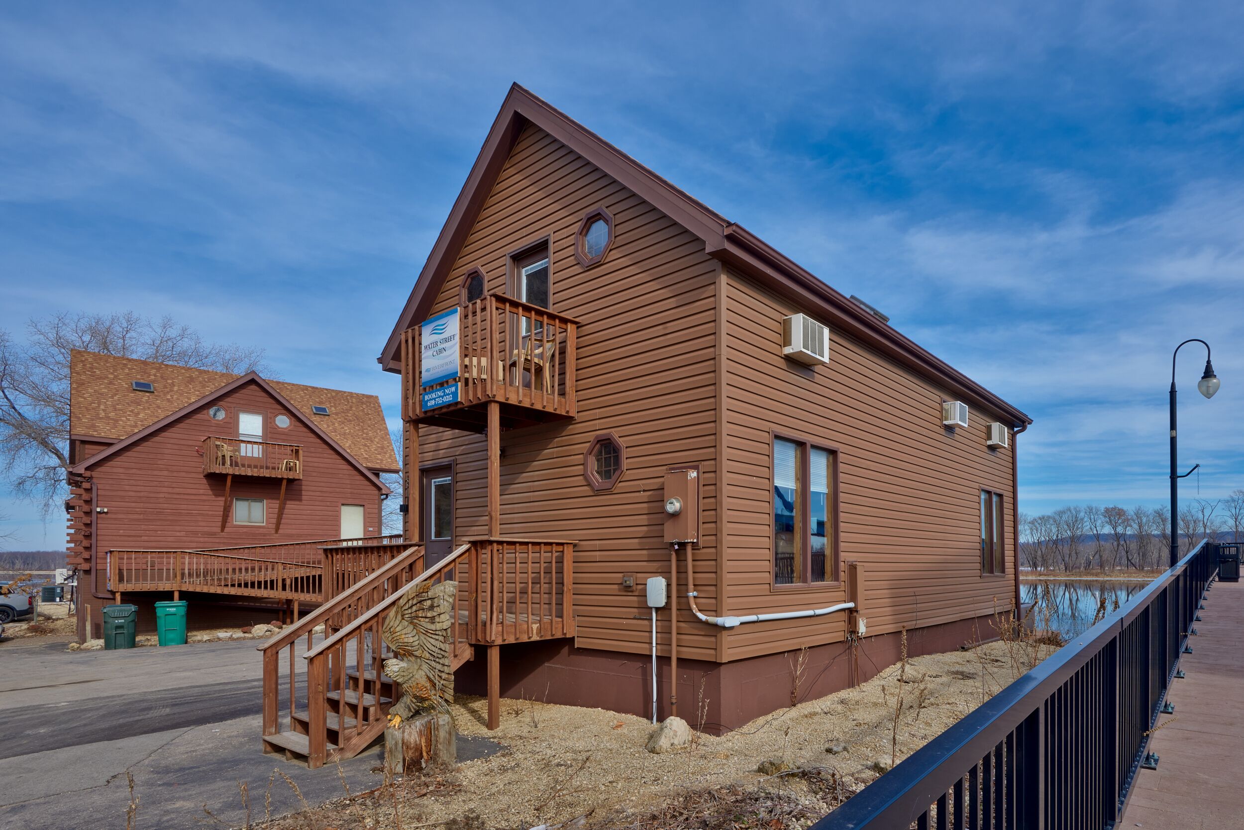 A wooden cabin with a balcony, a staircase, and a view of a body of water.