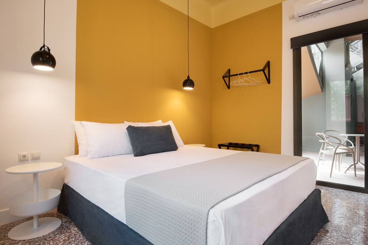 Et moderne hotelværelse med en stor seng, et rundt bord, en stol og en glasdør til et udendørs område.