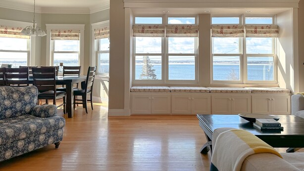 Un salón amplio con comedor, ventanas grandes con cortinas florales y vista al agua.
