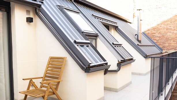 Een balkon met een houten stoel, een metalen hekwerk en een betegelde vloer.