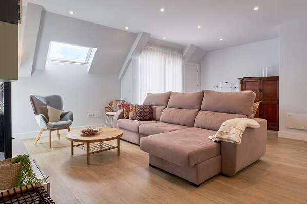 Un salon moderne avec un canapé d’angle, une table basse ronde et un fauteuil.