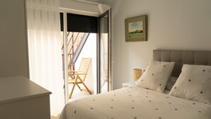 Een slaapkamer met een bed, een nachtkastje, een stoel en een raam met jaloezieën.